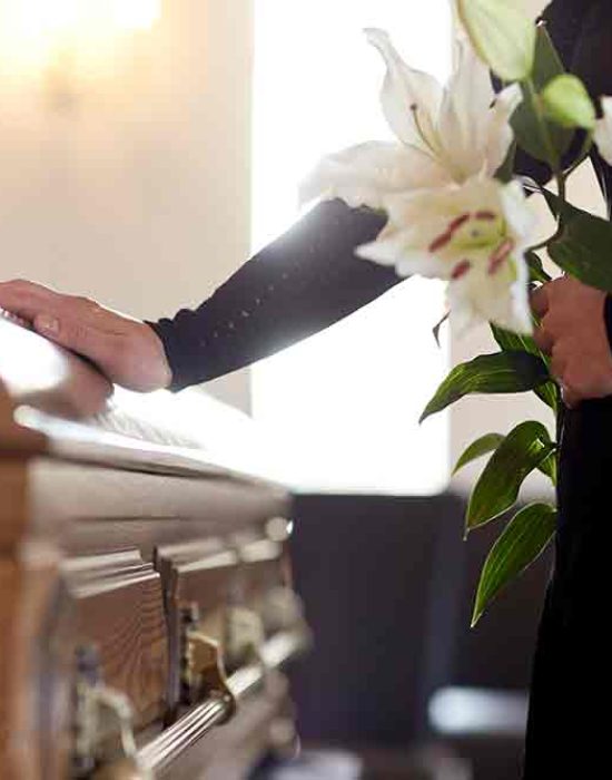 people and mourning concept - woman with white lily flowers and coffin at funeral in church